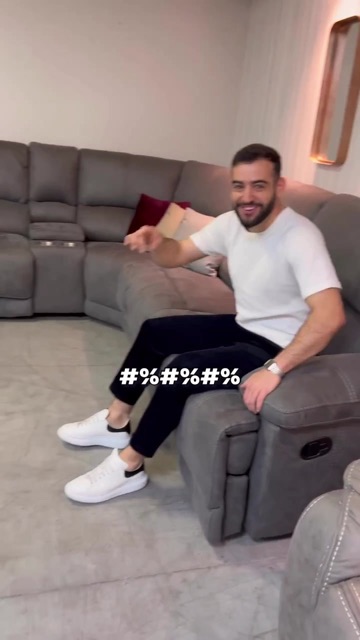 גבר בחולצה לבנה יושב על ספה פינתית אפורה נפתחת באולם תצוגה, קאבר רילס