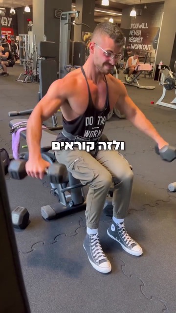 גבר שרירי מתאמן עם משקולות יד על ספסל בחדר כושר, קאבר רילס עם הכיתוב "ולזה קוראים"